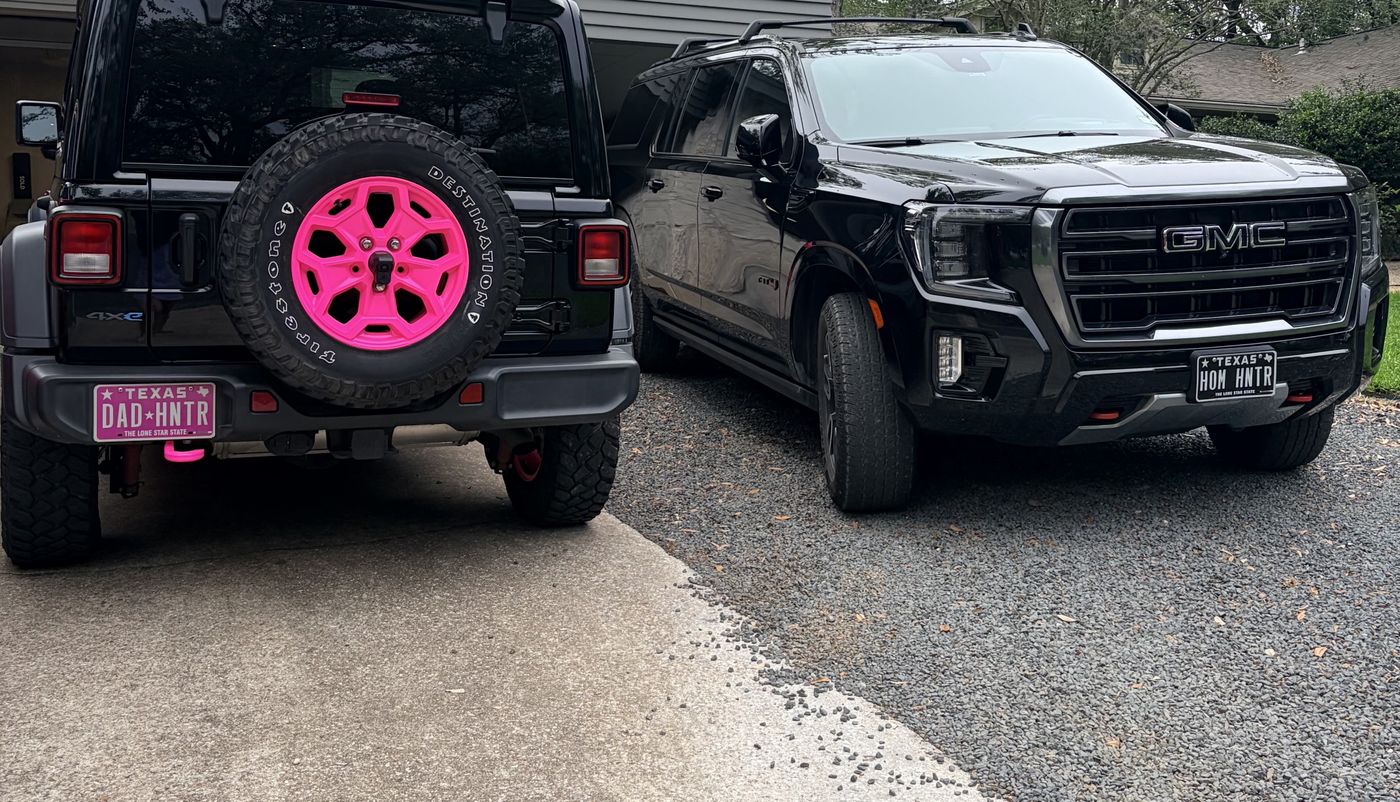 Pink-accented Jeep with a pink DAD HNTR plate parked next to a black GMC with a HOM HNTR plate