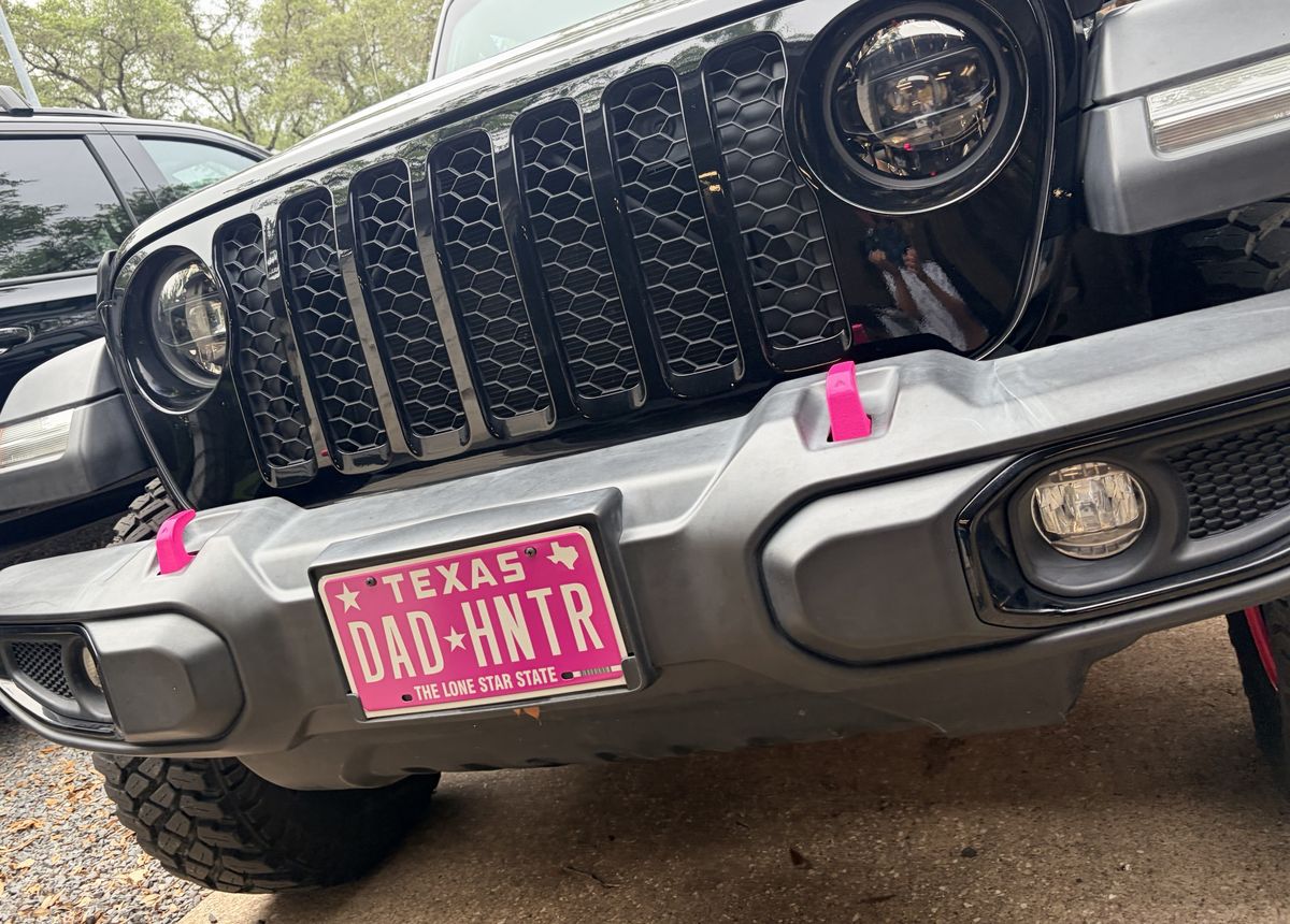 Front of a black Jeep with pink tow hooks and a pink DAD HNTR Texas plate